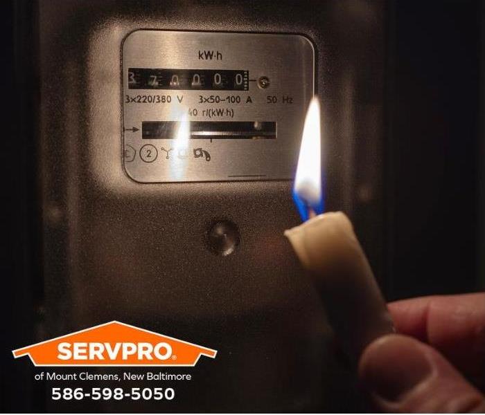 A person holds a candle up to read a meter during a power outage.