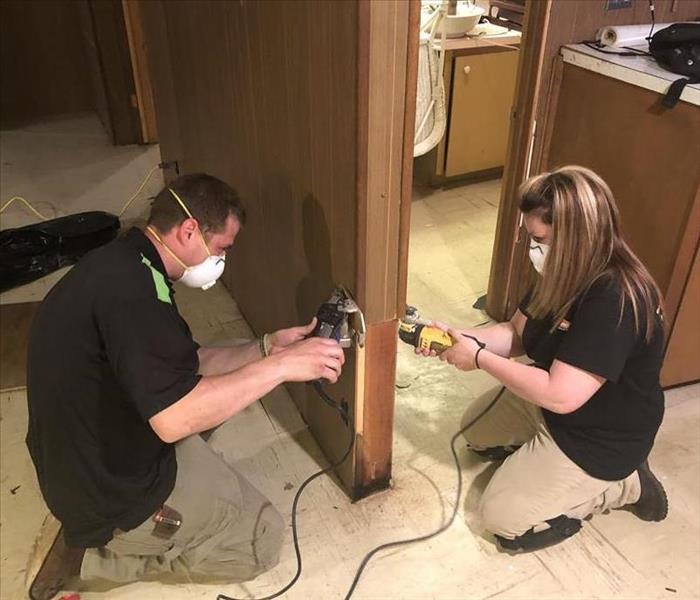 male and female SERVPRO employees cutting walls at 2' from the ground