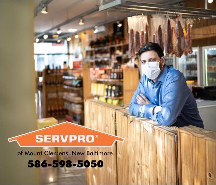 A business owner stands at the counter of his small business with a facemask on.