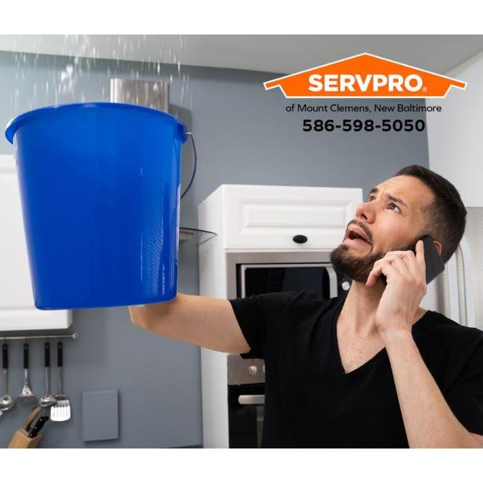 A person holds a bucket up to catch water dripping from the ceiling.